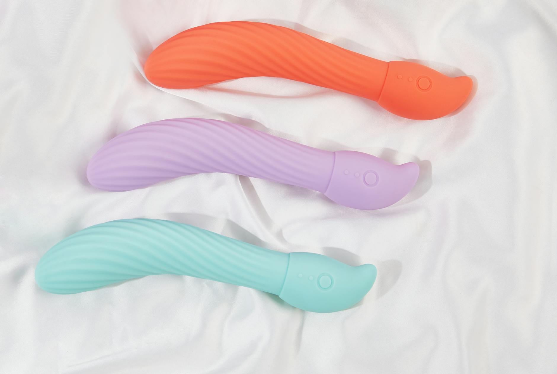 Three colorful clitoral vibrators arranged on white fabric, showing smooth texture and design details