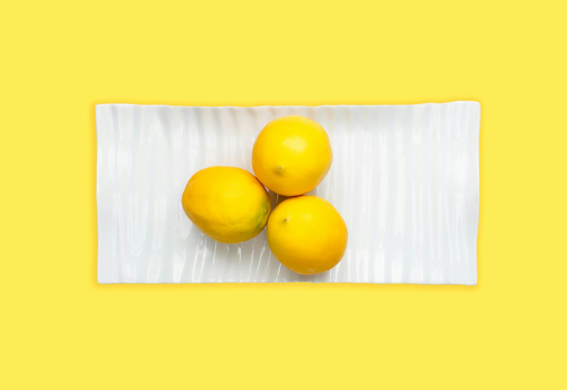A yellow silicone vibrator surrounded by fresh fruit on a bright background, symbolizing gentleness and self-care.