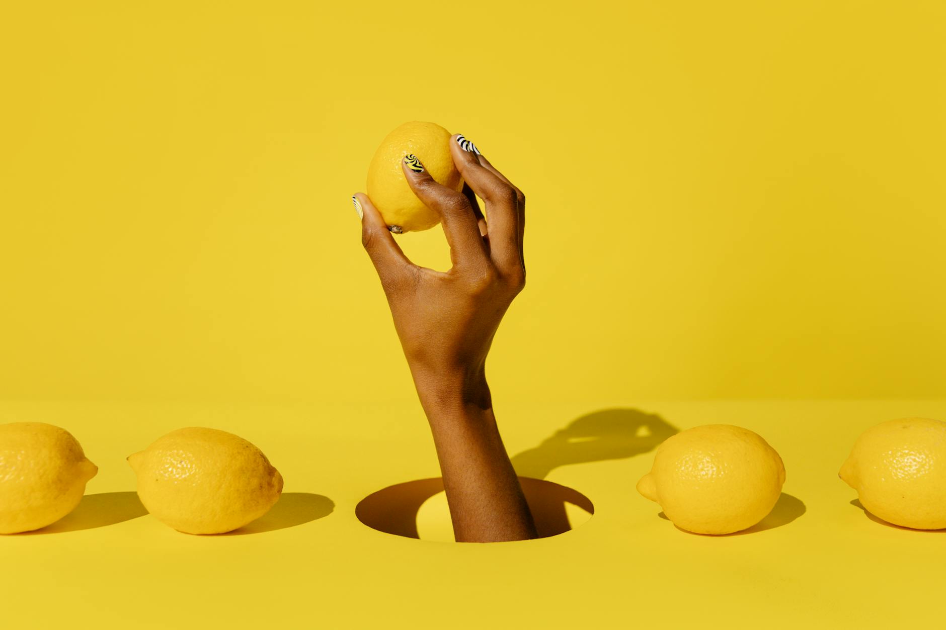 Hand holding a fresh lemon against a vivid yellow background, symbolizing renewal and natural sensation