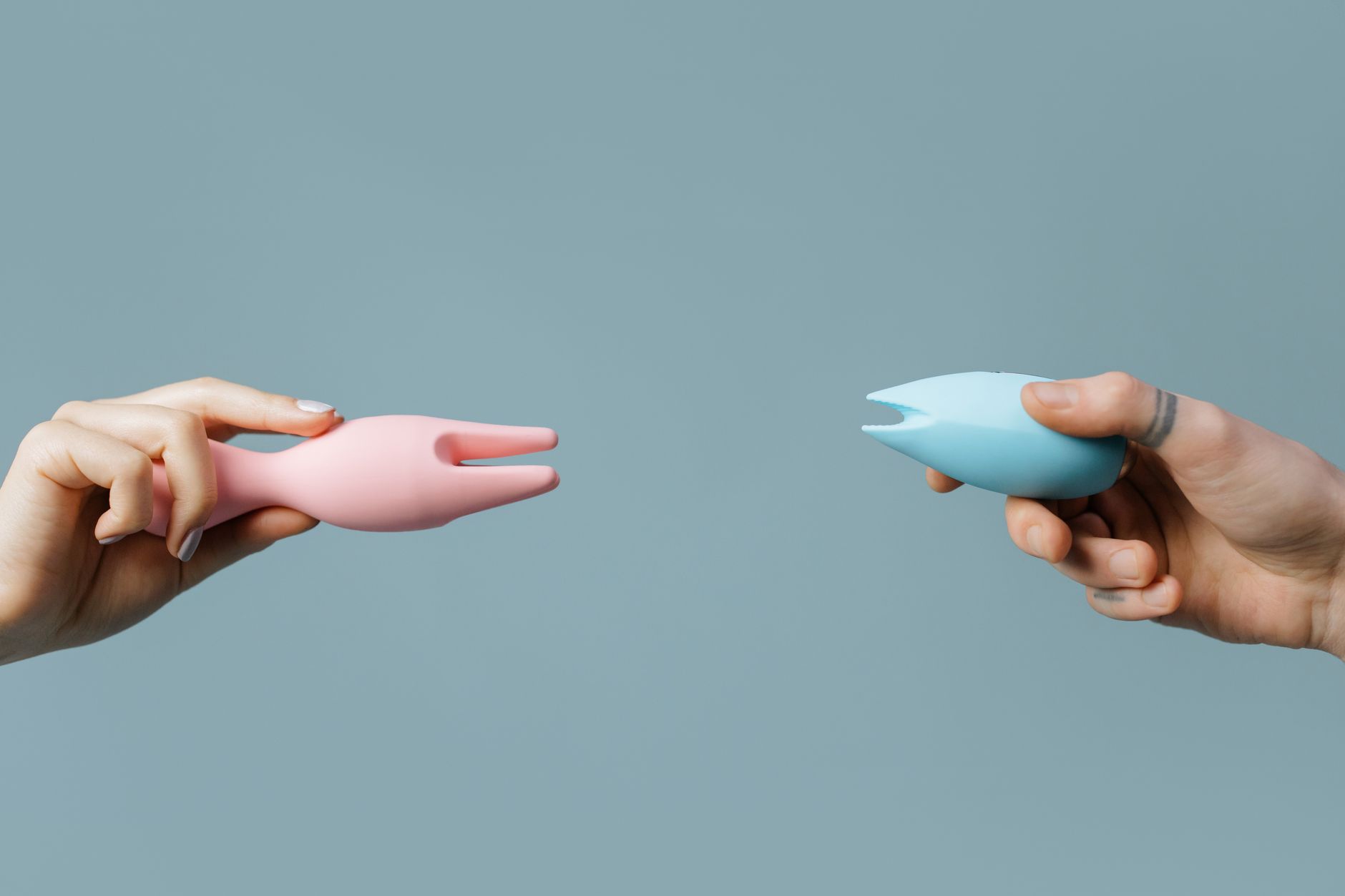 Close-up of hands holding pastel silicone vibrators against a soft background