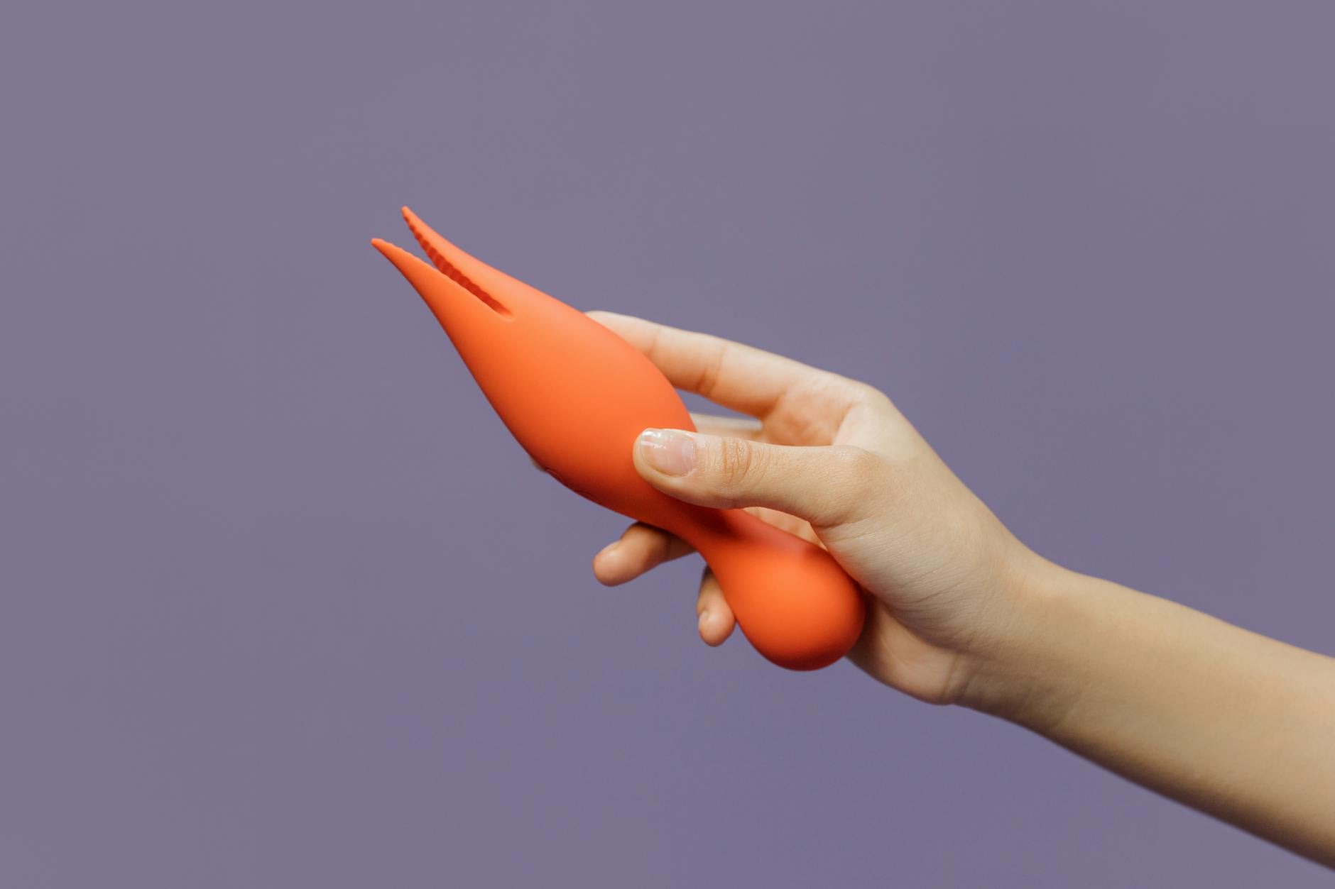 A hand holding a yellow silicone lemon vibrator against a minimalist purple backdrop, showcasing smooth body-safe design.