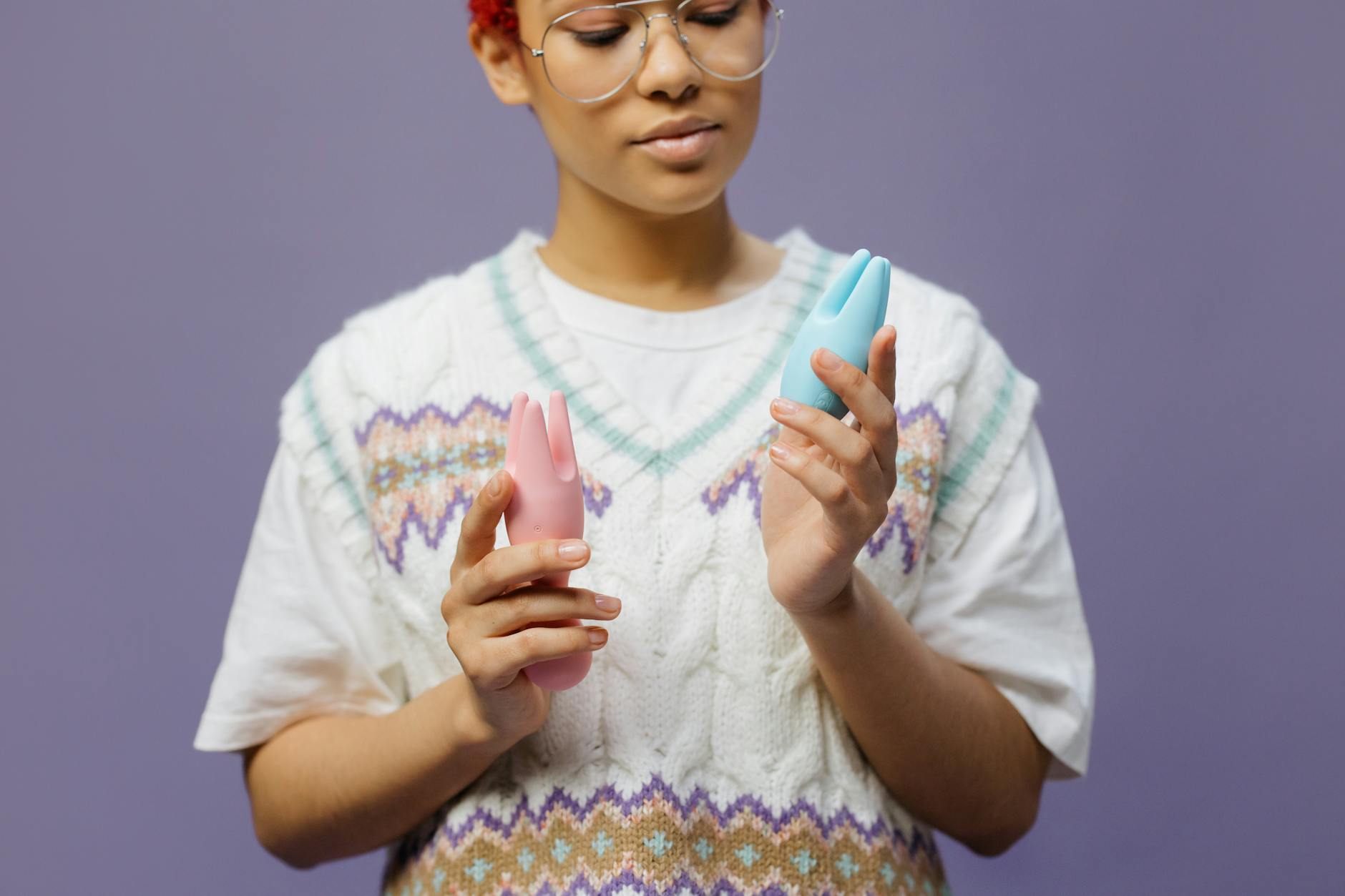 Woman in contemplative moment holding blue and pink clitoral vibrators, representing post-surgical recovery and gentle pleasure.